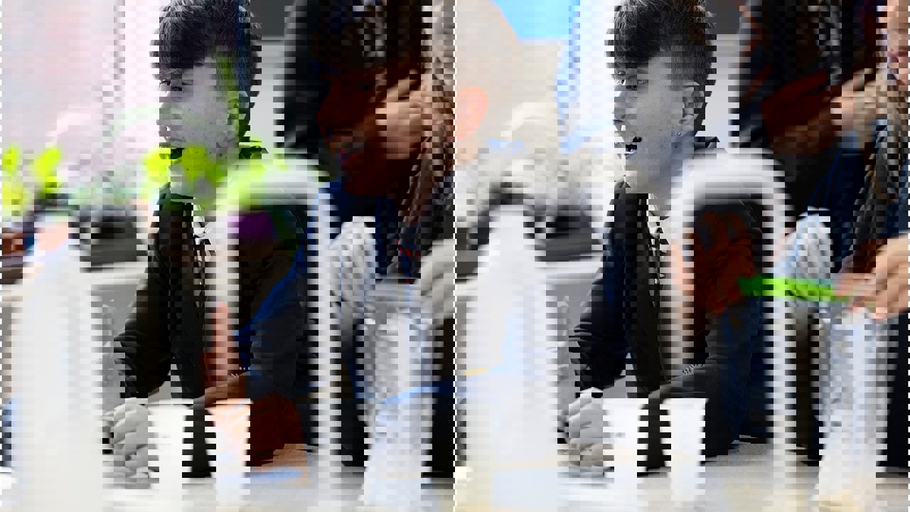 A student in a school science lab smiles as others at his bench work with equipment such as beakers, liquids and chemicals.